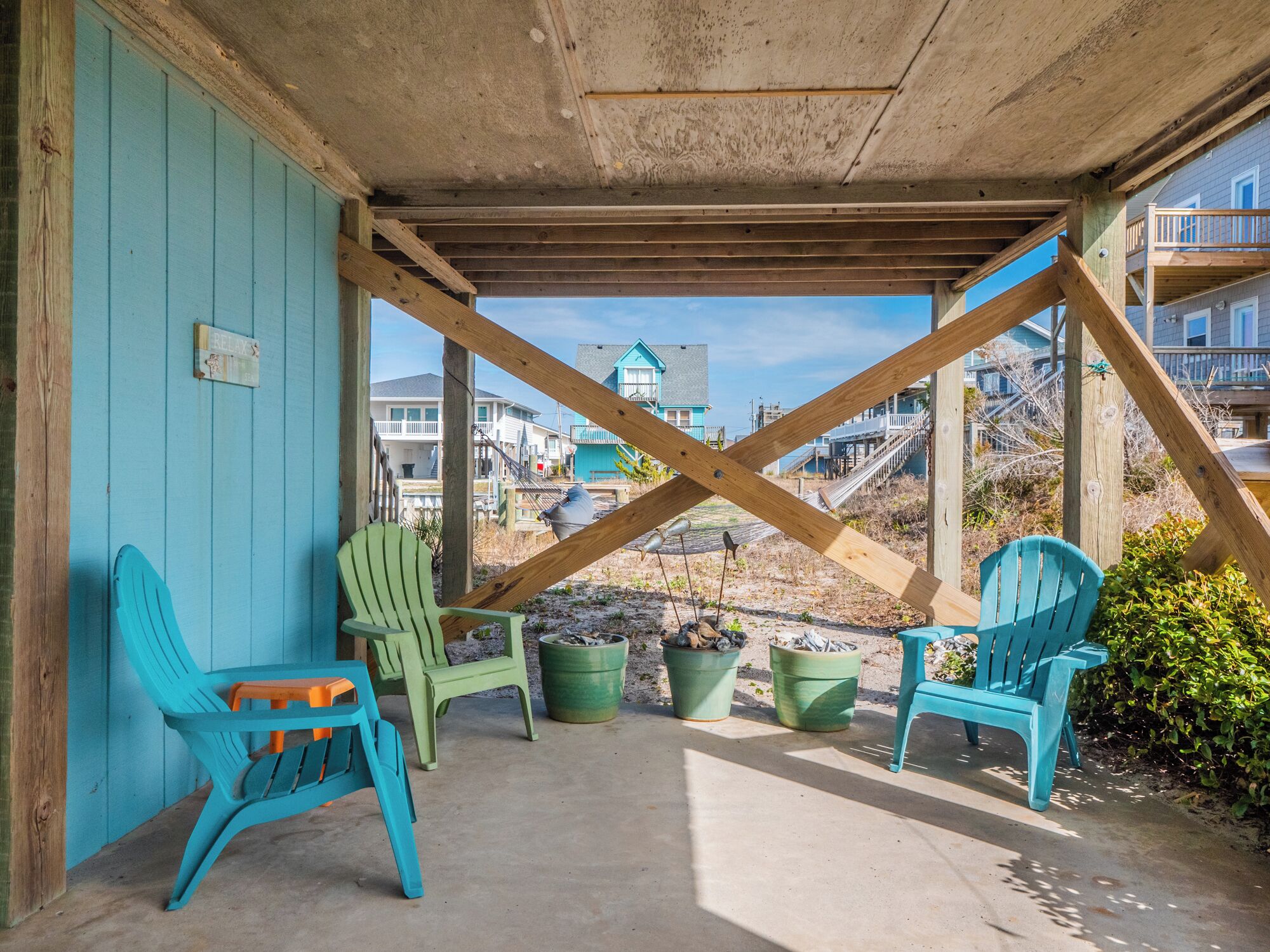 A covered outdoor seating area with turquoise chairs and planters.