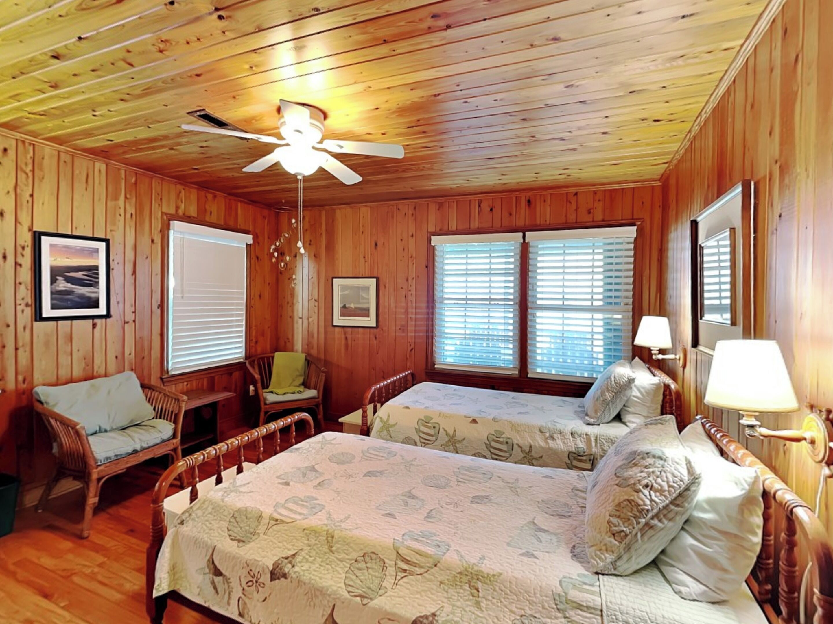 A cabin with two beds, a ceiling fan, wooden walls, and a window with blinds.