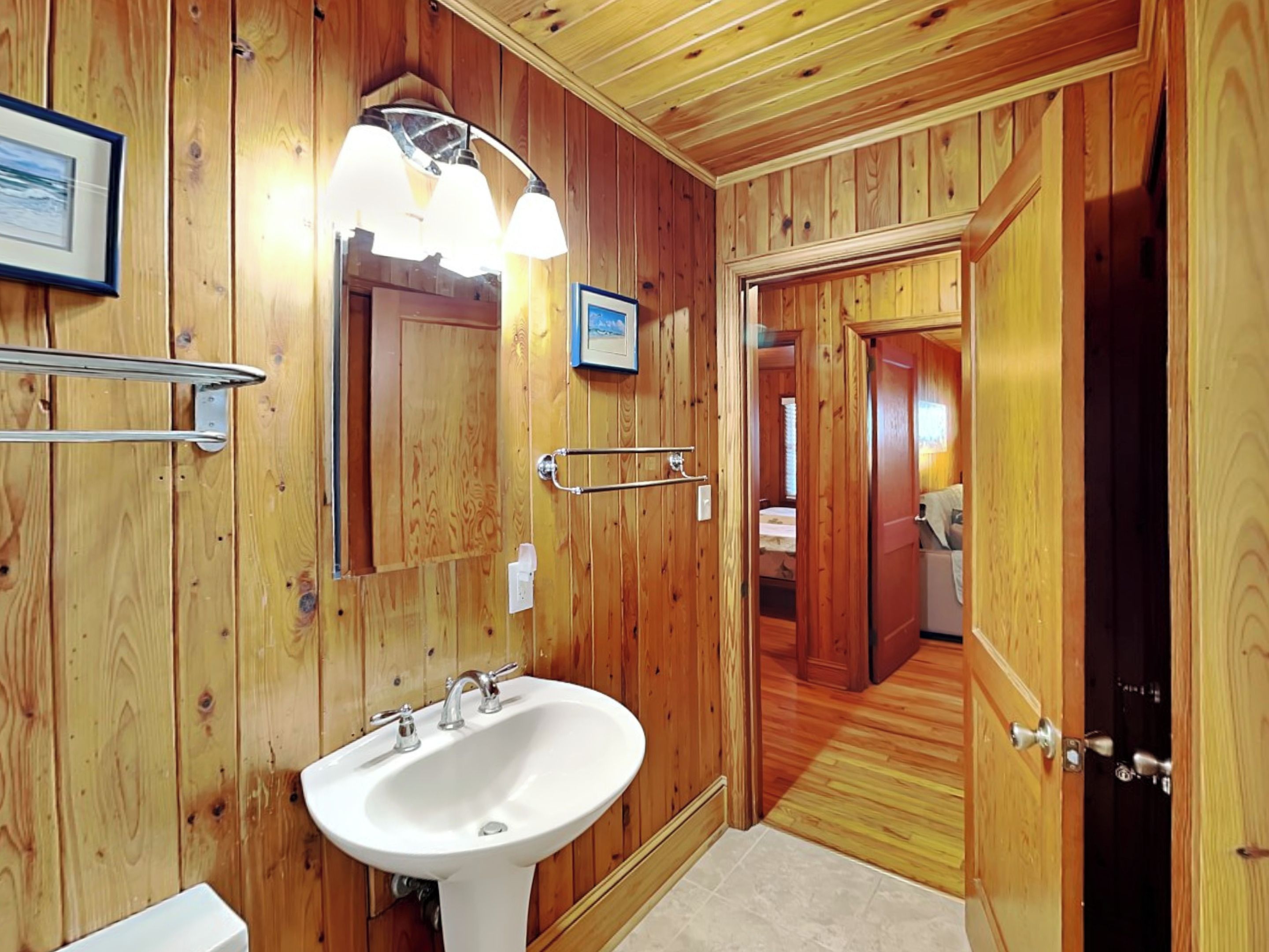 A wooden-paneled bathroom with a white sink, a towel rack, and a framed picture on the wall.