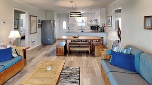 Un salon moderne avec une table basse en bois, des canapés bleus et une cuisine en arrière-plan.