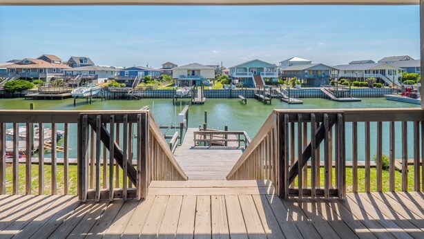 Une terrasse en bois offrant une vue sur un port de plaisance et sur des maisons en arrière-plan.