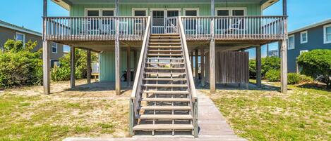 A beachfront house with a wooden staircase leading to a balcony.