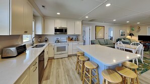 A modern kitchen with white cabinets, a central island with stools, a microwave, and a stove.