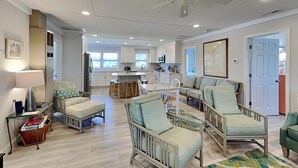 A spacious living area with a kitchen in the background, a dining area with stools, and a large window providing natural light.