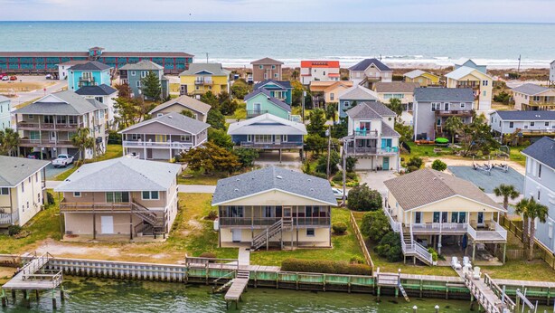 A coastal residential area with houses, a dock, and a beach in the background.