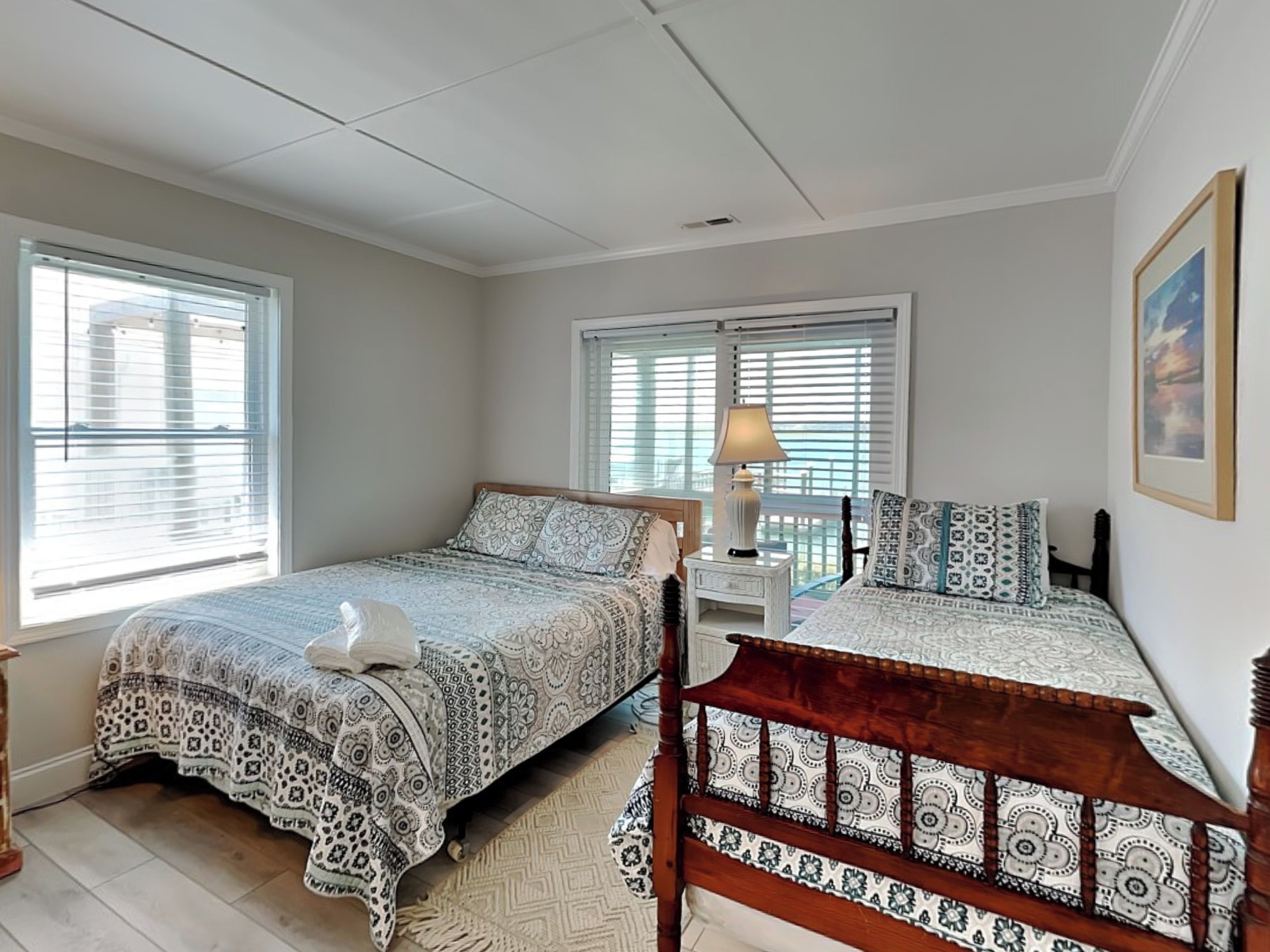 A bedroom with two beds, a nightstand with a lamp, and a framed picture on the wall.