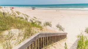 Une plage avec une promenade en bois menant au rivage, une plage de sable et l’océan.