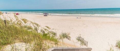 A beach with a wooden boardwalk leading to the shore, sandy beach, and ocean.