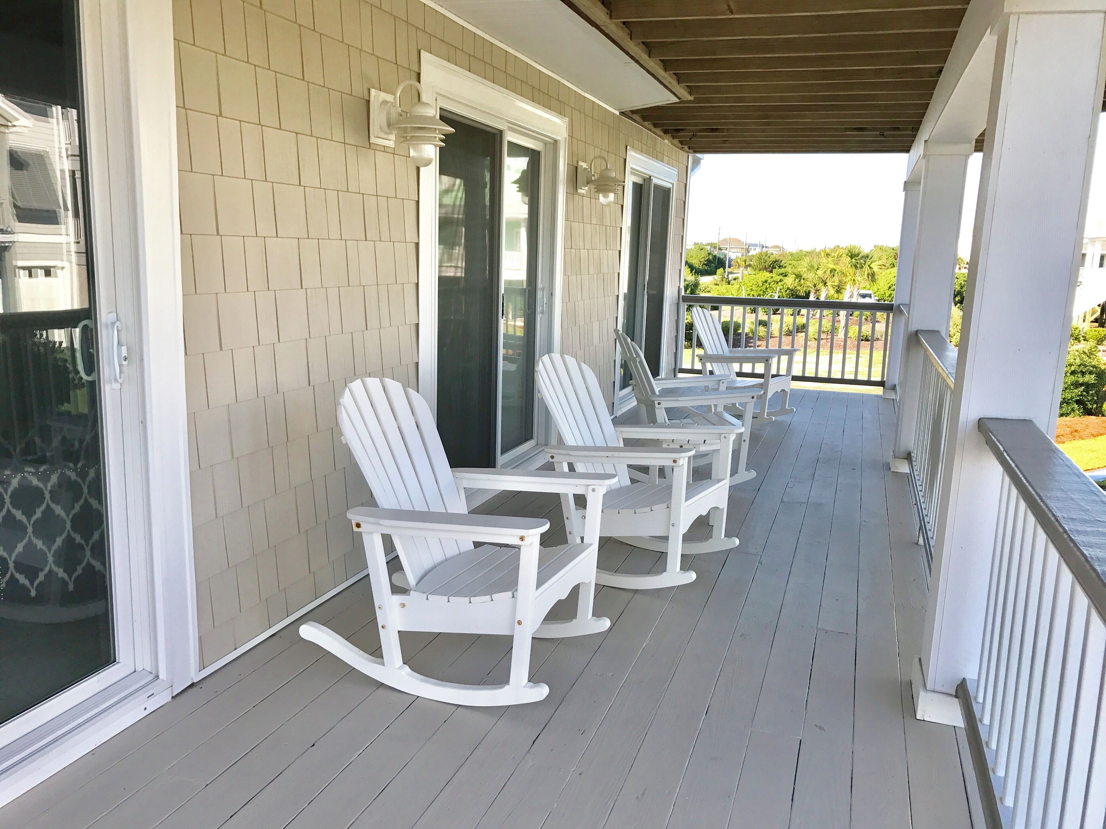 A covered porch with white rocking chairs and a glass door.