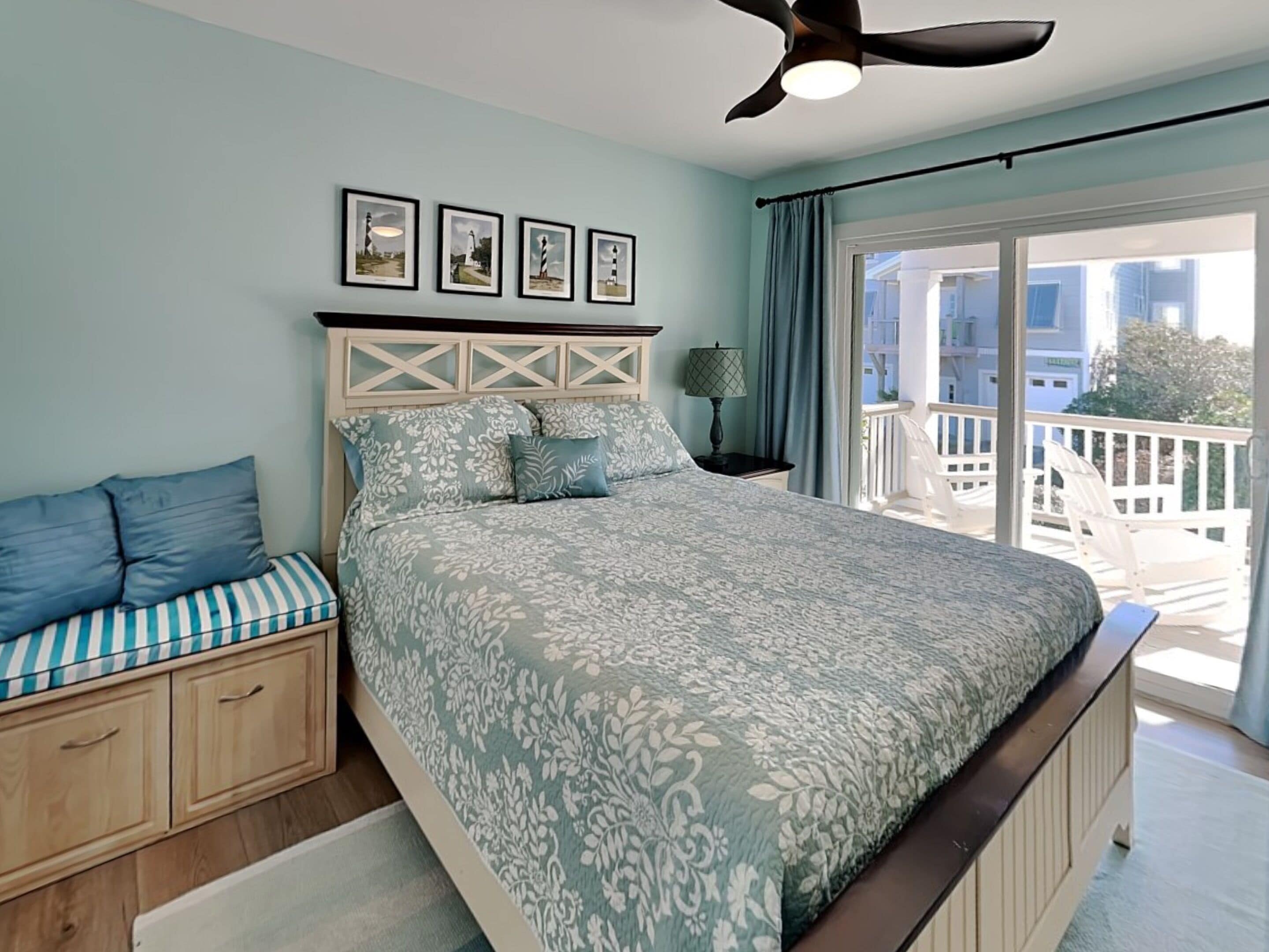 A bedroom with a bed, a nightstand, a lamp, a ceiling fan, and a view of the outside balcony.