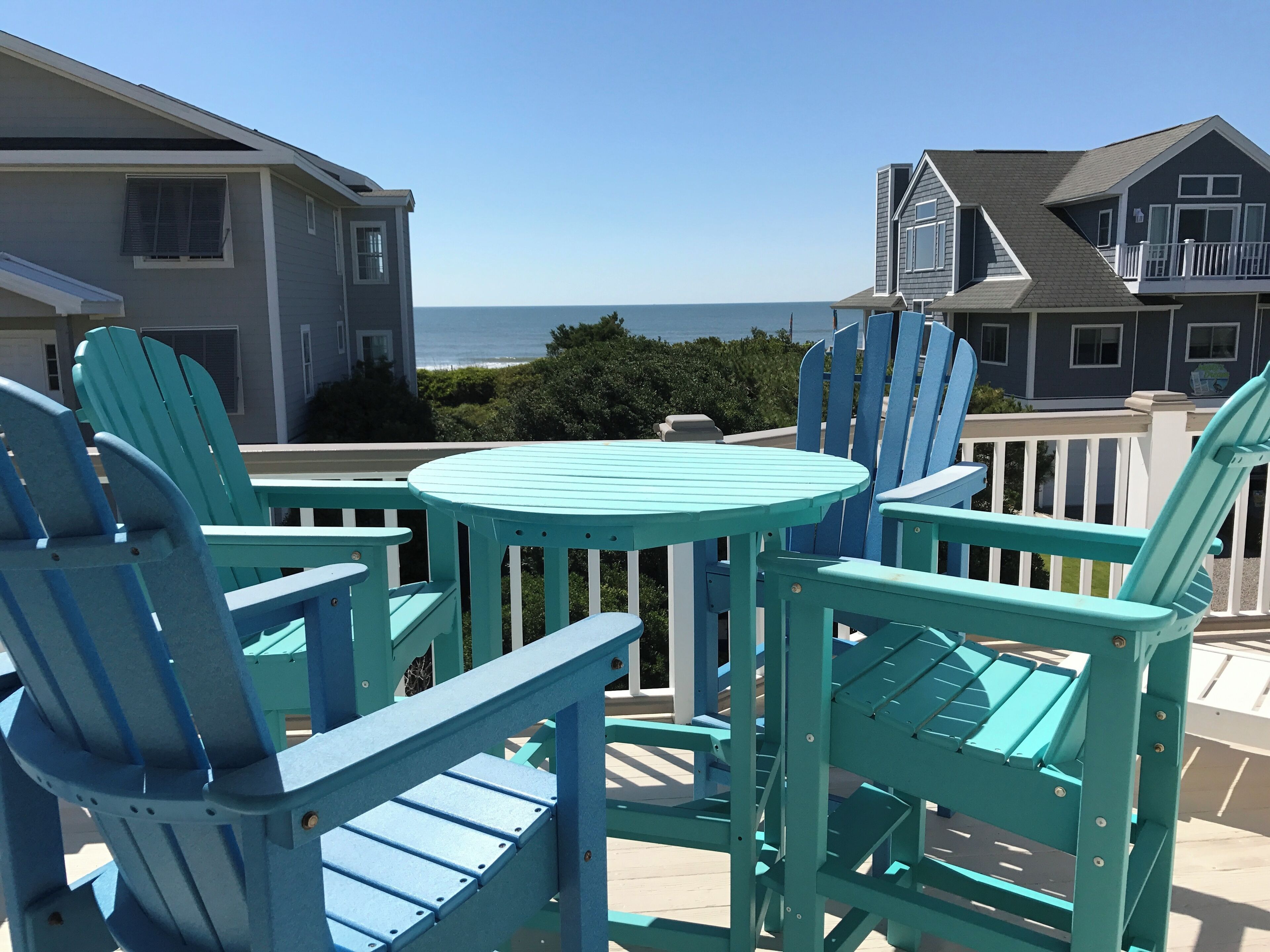 Un patio con sillones Adirondack turquesa y una pequeña mesa redonda, con vista a una zona residencial y al océano.