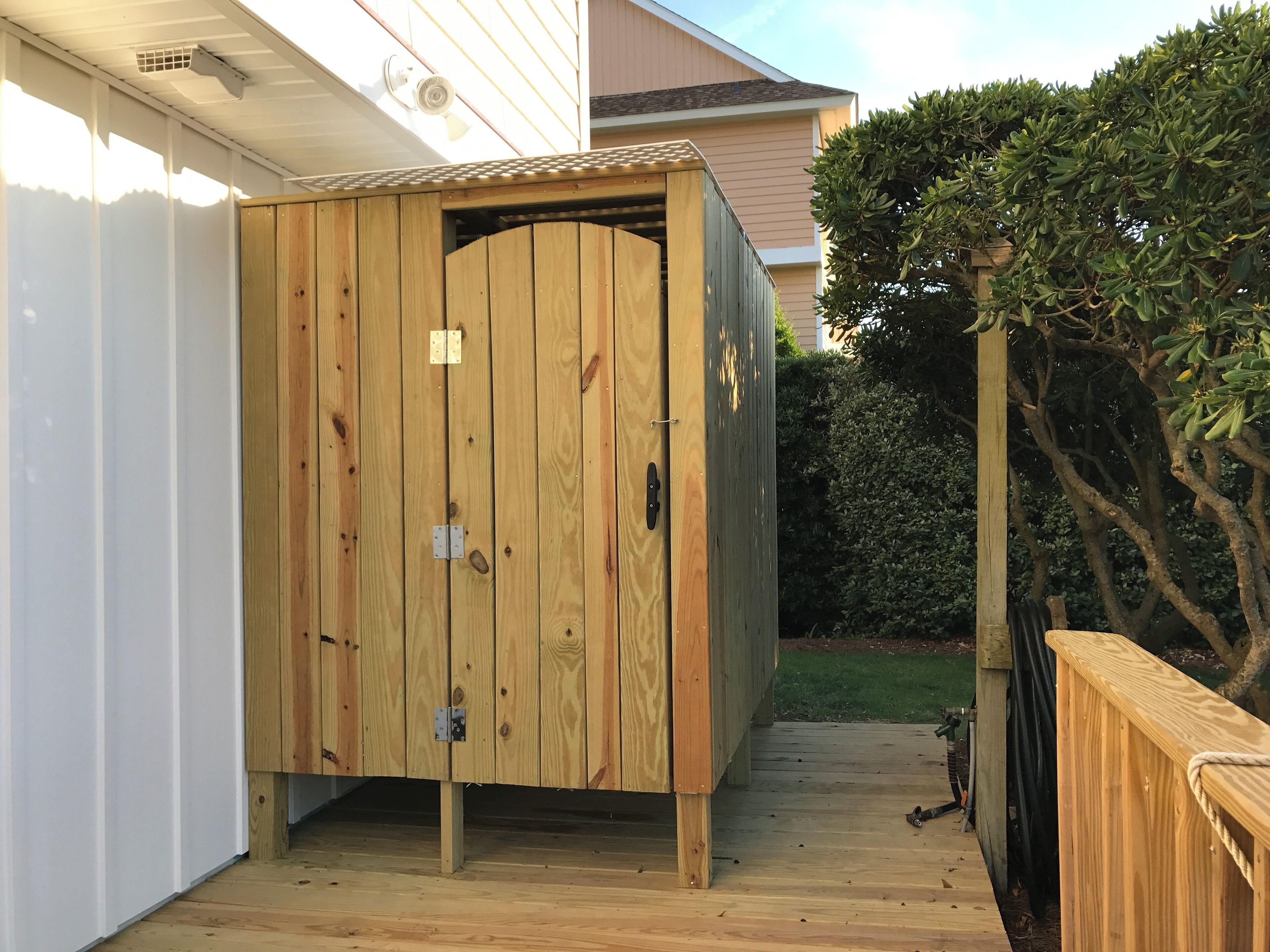 A wooden shed with a door, positioned on a wooden deck adjacent to a house.