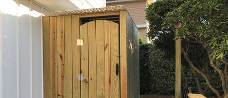 A wooden shed with a door, positioned on a wooden deck adjacent to a house.