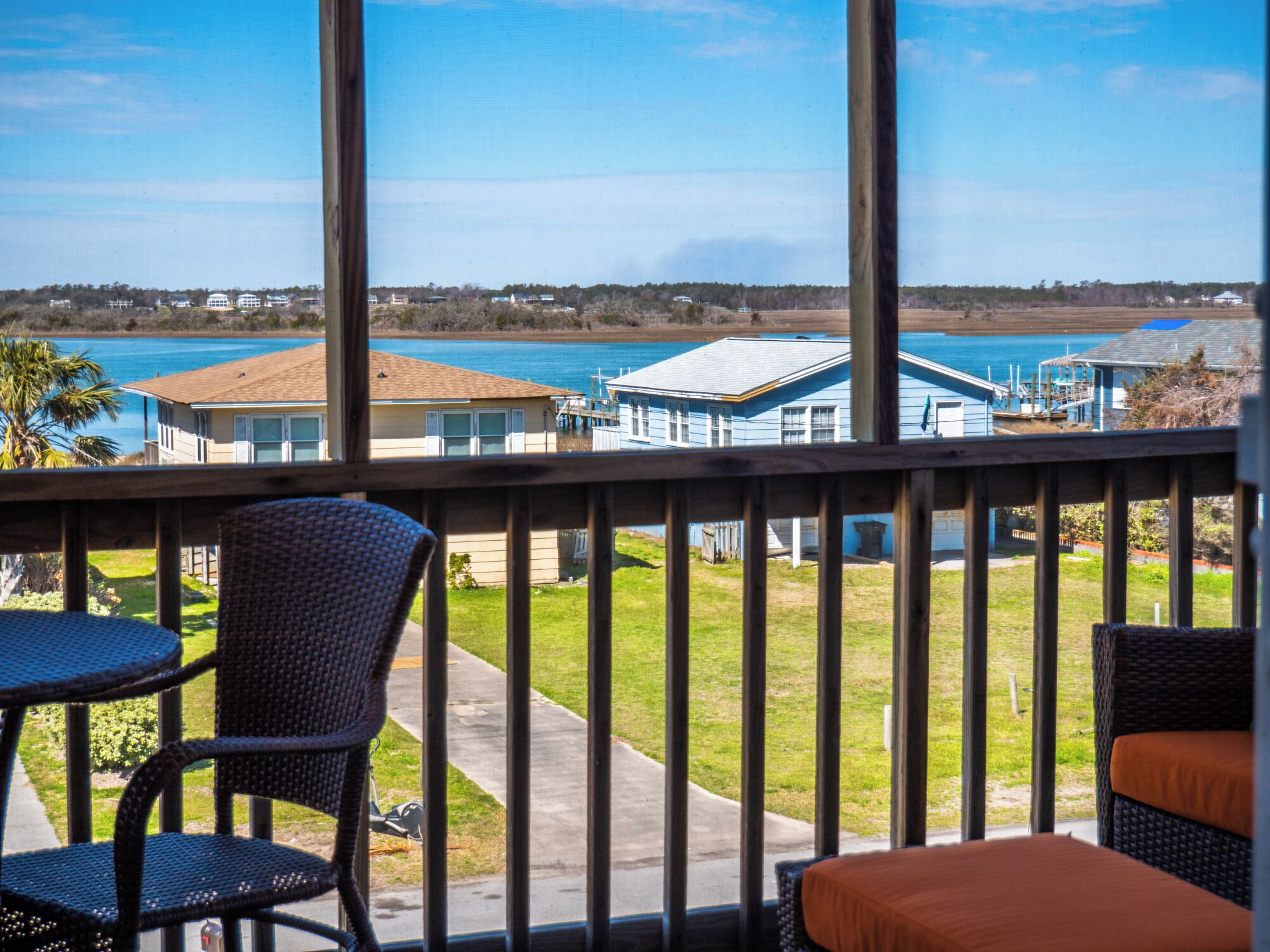 Een balkon met rieten stoelen en uitzicht op een meer en huizen.