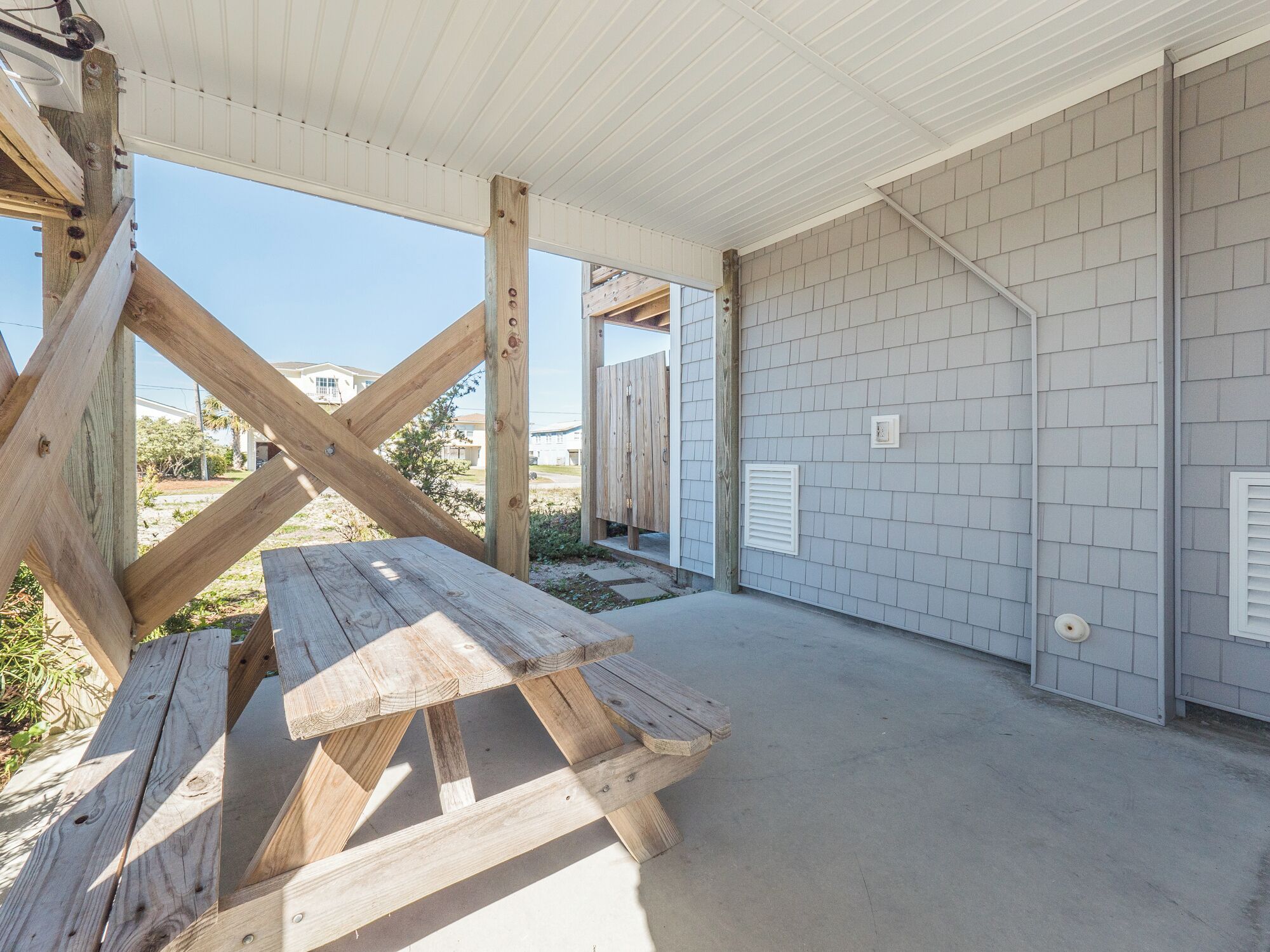 A covered outdoor area with a wooden picnic table, a metal roof, and a tiled wall.