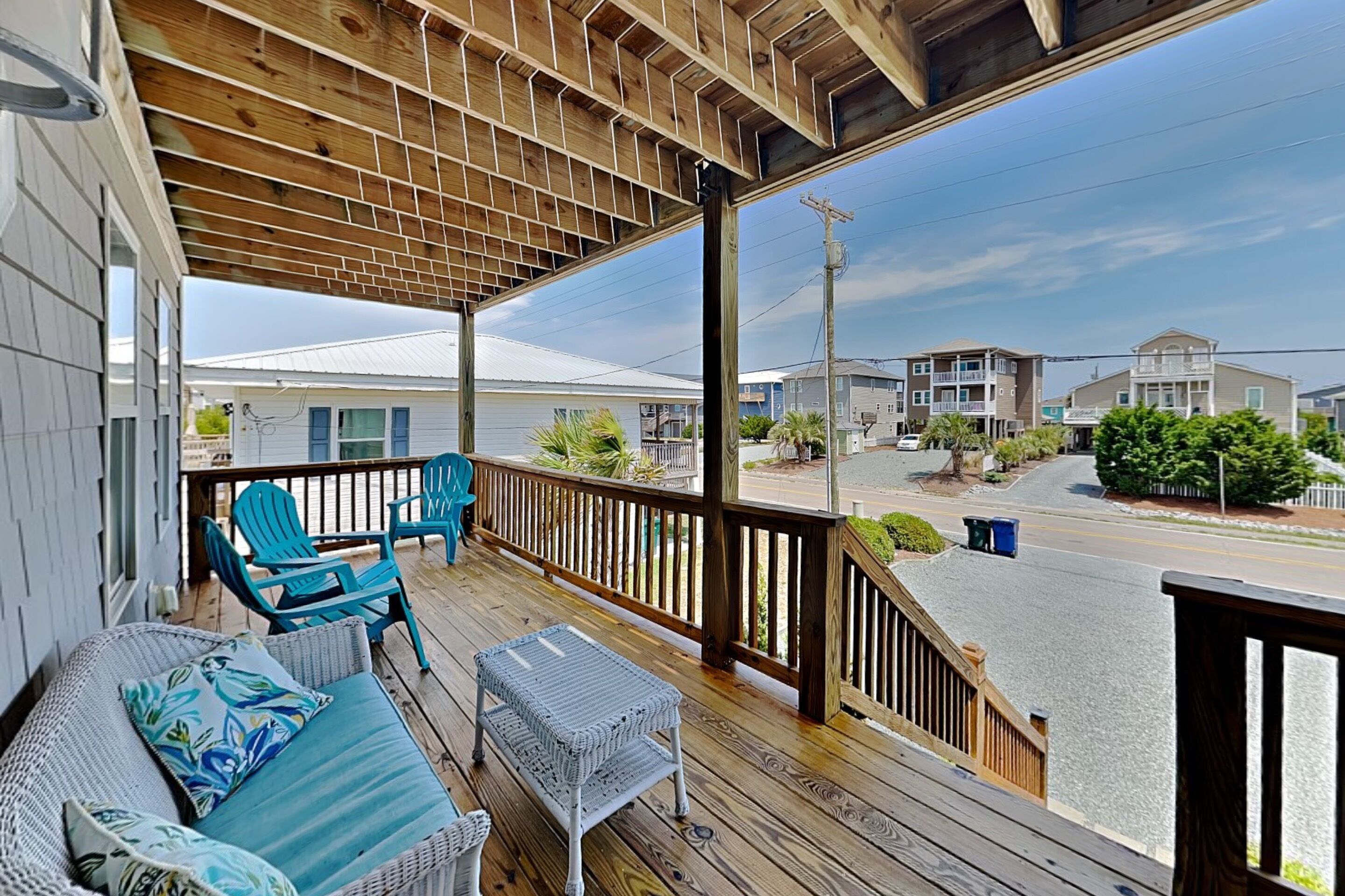 A covered porch with wicker furniture, a small table, and a view of the street and neighboring buildings.