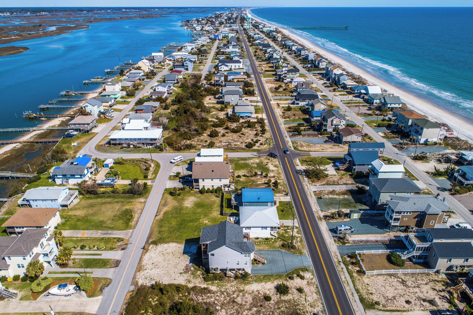 Vue aérienne d’une zone résidentielle côtière, avec des maisons, des routes et une plage.