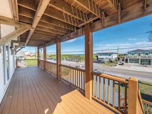 A wooden deck with a railing, overlooking a street with houses and a clear sky.