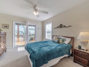 A bedroom with a bed, a nightstand, a dresser, a ceiling fan, and a view through a glass door to the outside.