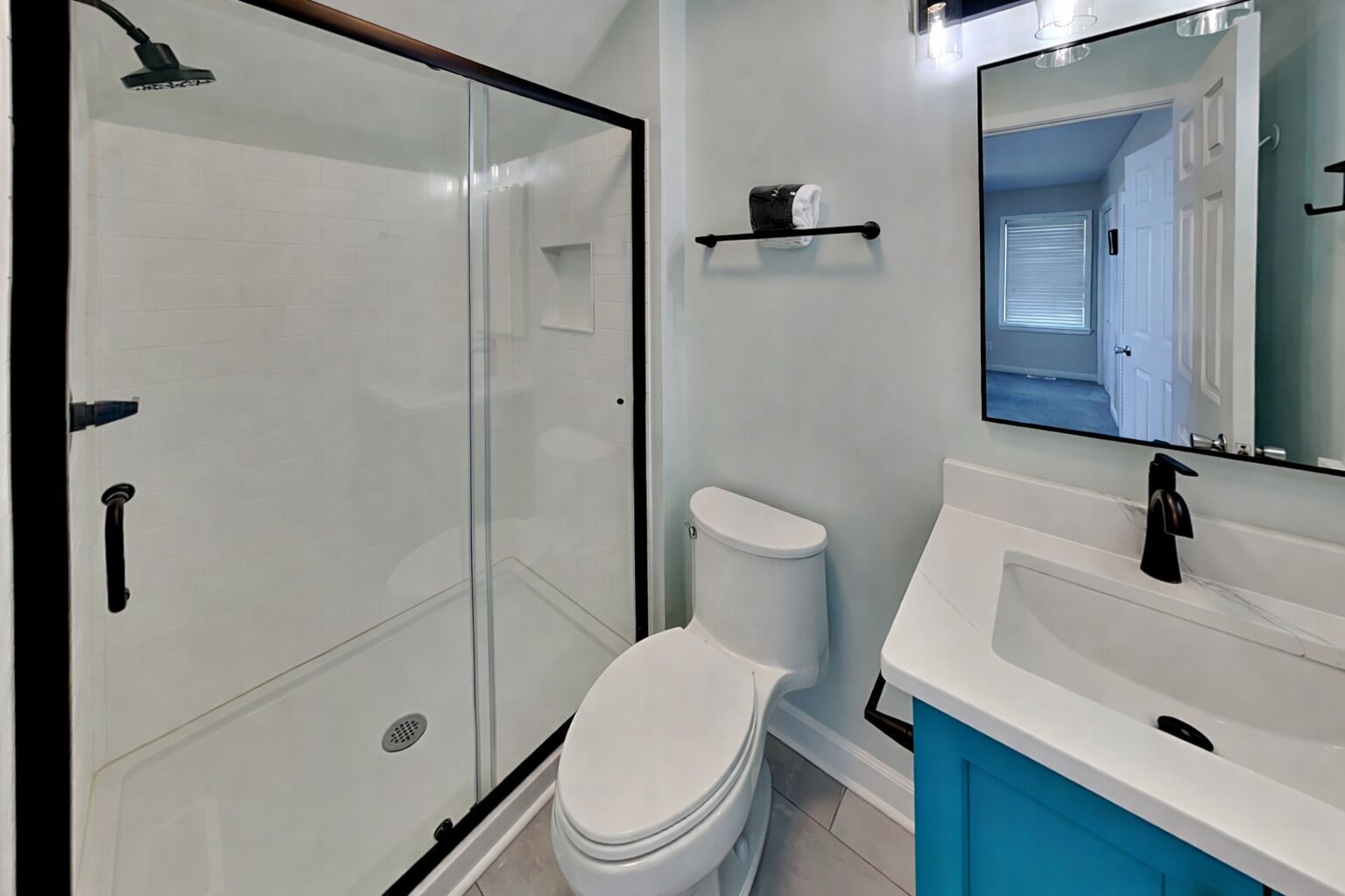 Une salle de bain avec une douche à parois de verre, des toilettes blanches, un lavabo avec un robinet noir et un miroir.