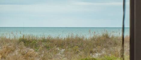 A view of a beach with a grassy foreground and a calm sea under a cloudy sky.