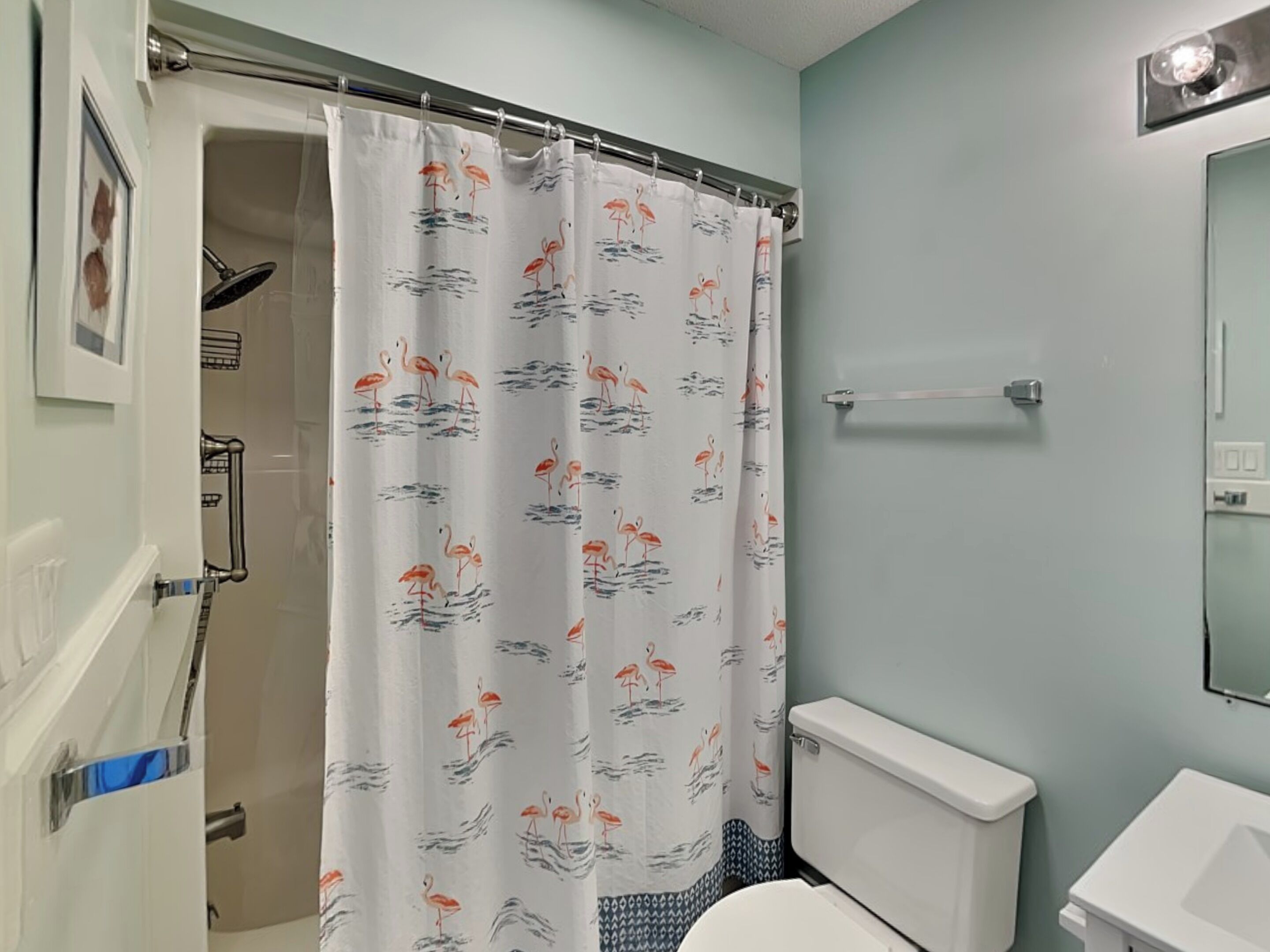 Un baño con inodoro, cortina de ducha con estampado de flamenco y pared azul claro.