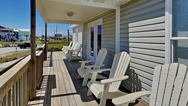 Eine Holzterrasse mit Adirondack-Stühlen, einer Veranda und Blick auf die Straße.