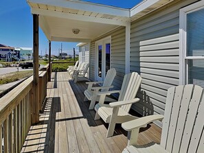 Una terraza de madera con sillas Adirondack, un porche cubierto y vistas a la calle.