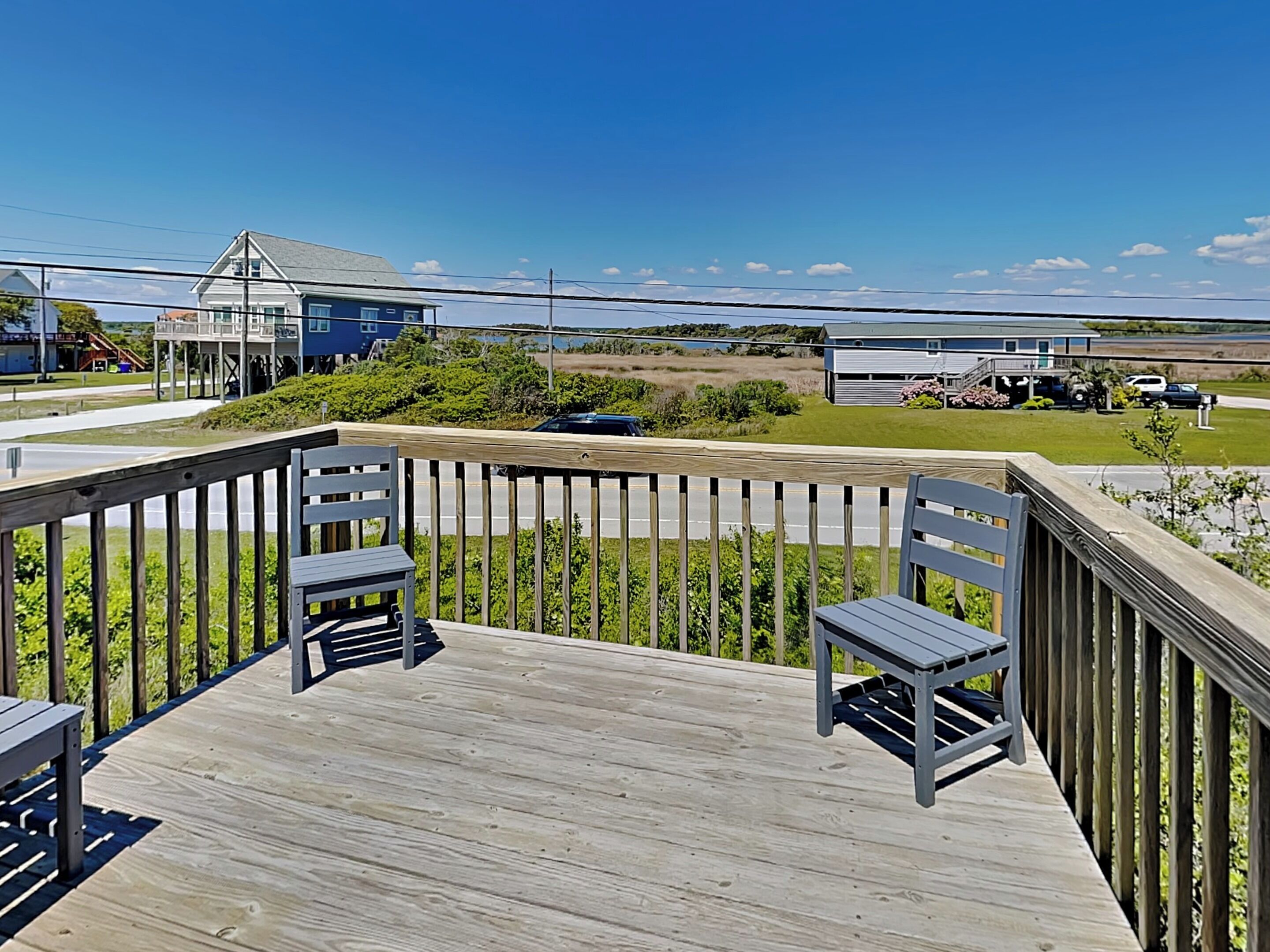 A wooden deck with two chairs and a table, overlooking a road and houses.