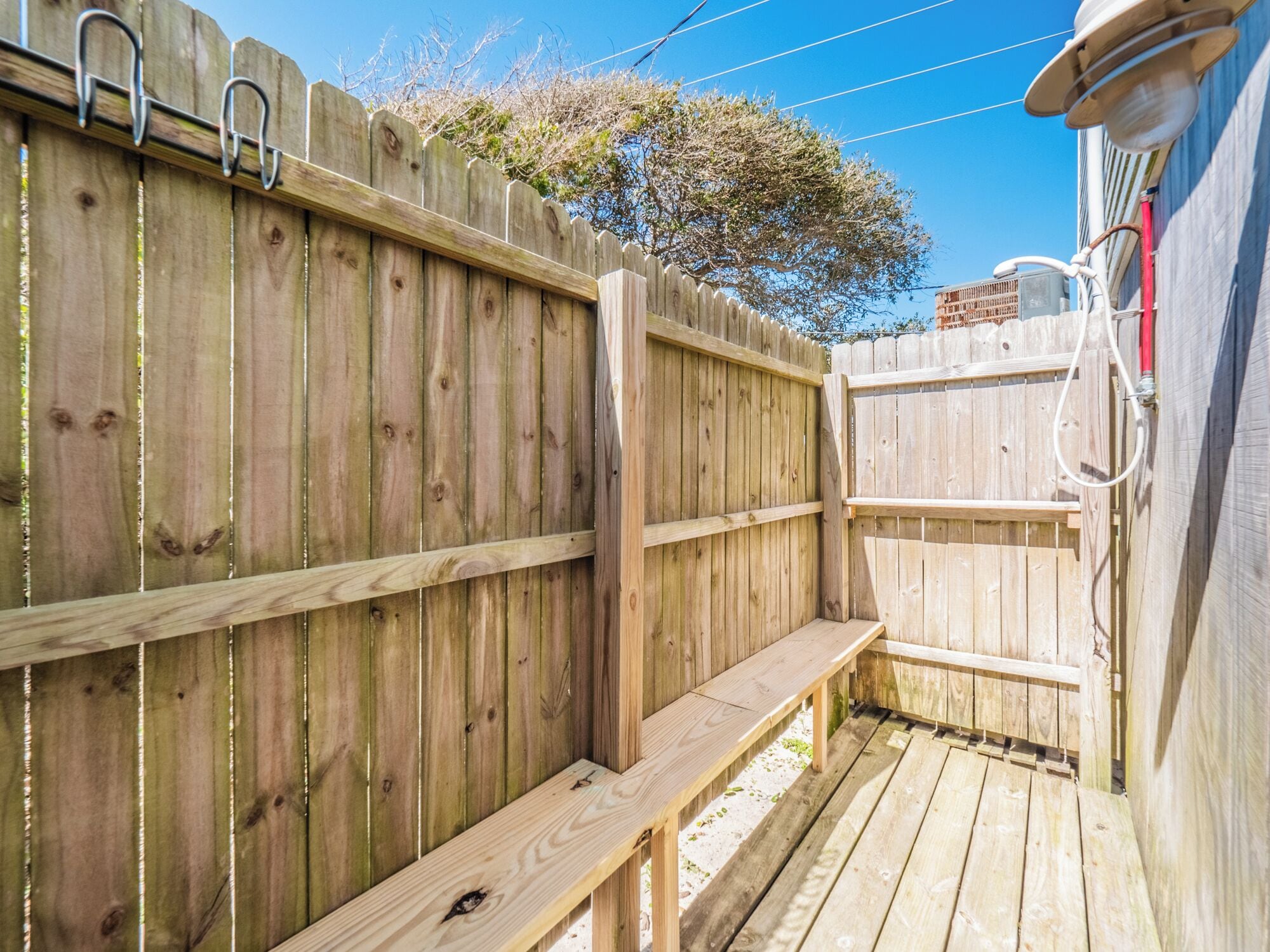 A wooden deck with a bench and a hose attached to the fence.
