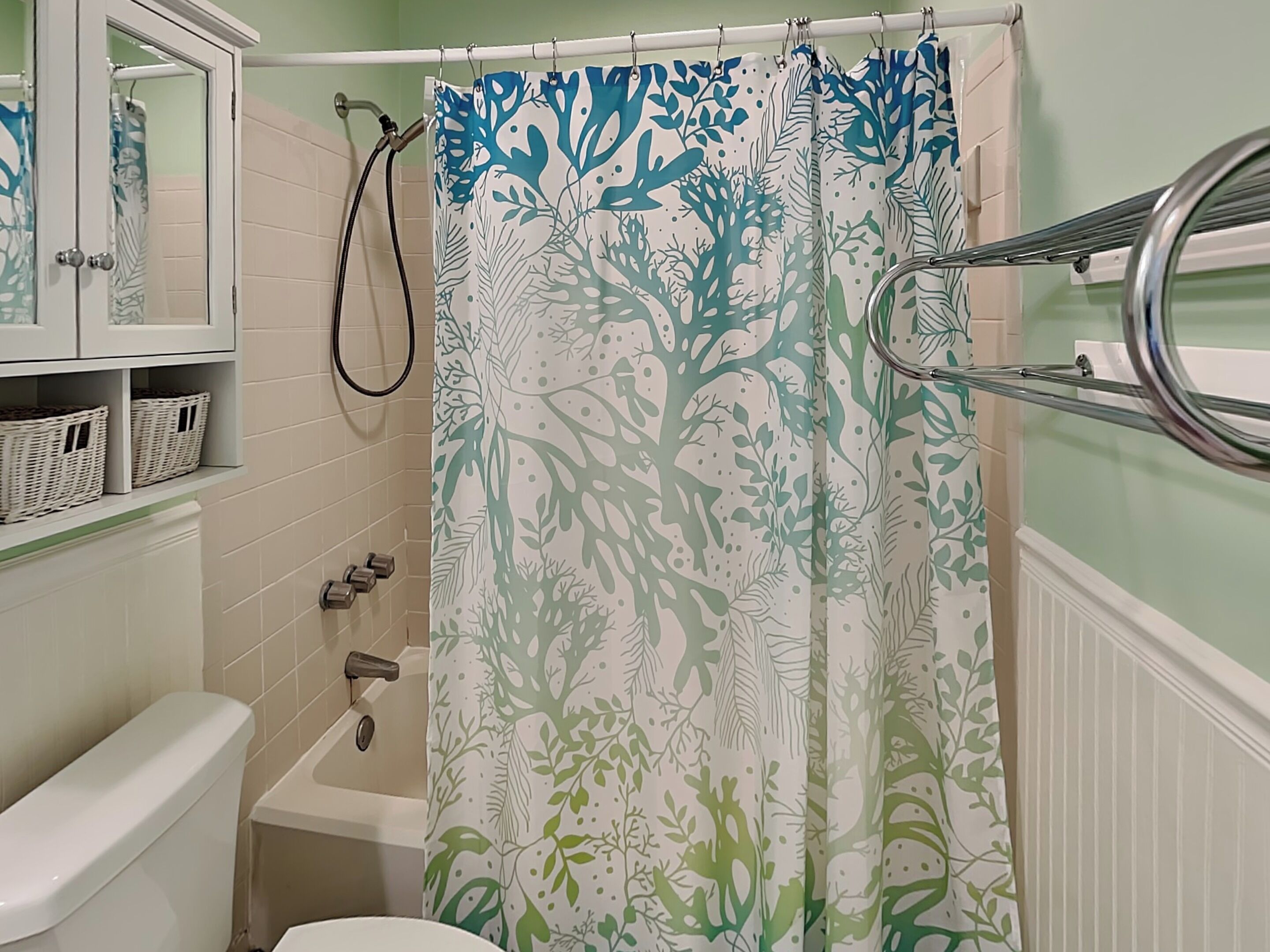 Un bagno con il water, una vasca da bagno, una tenda da doccia con motivo a foglie e un portascope.