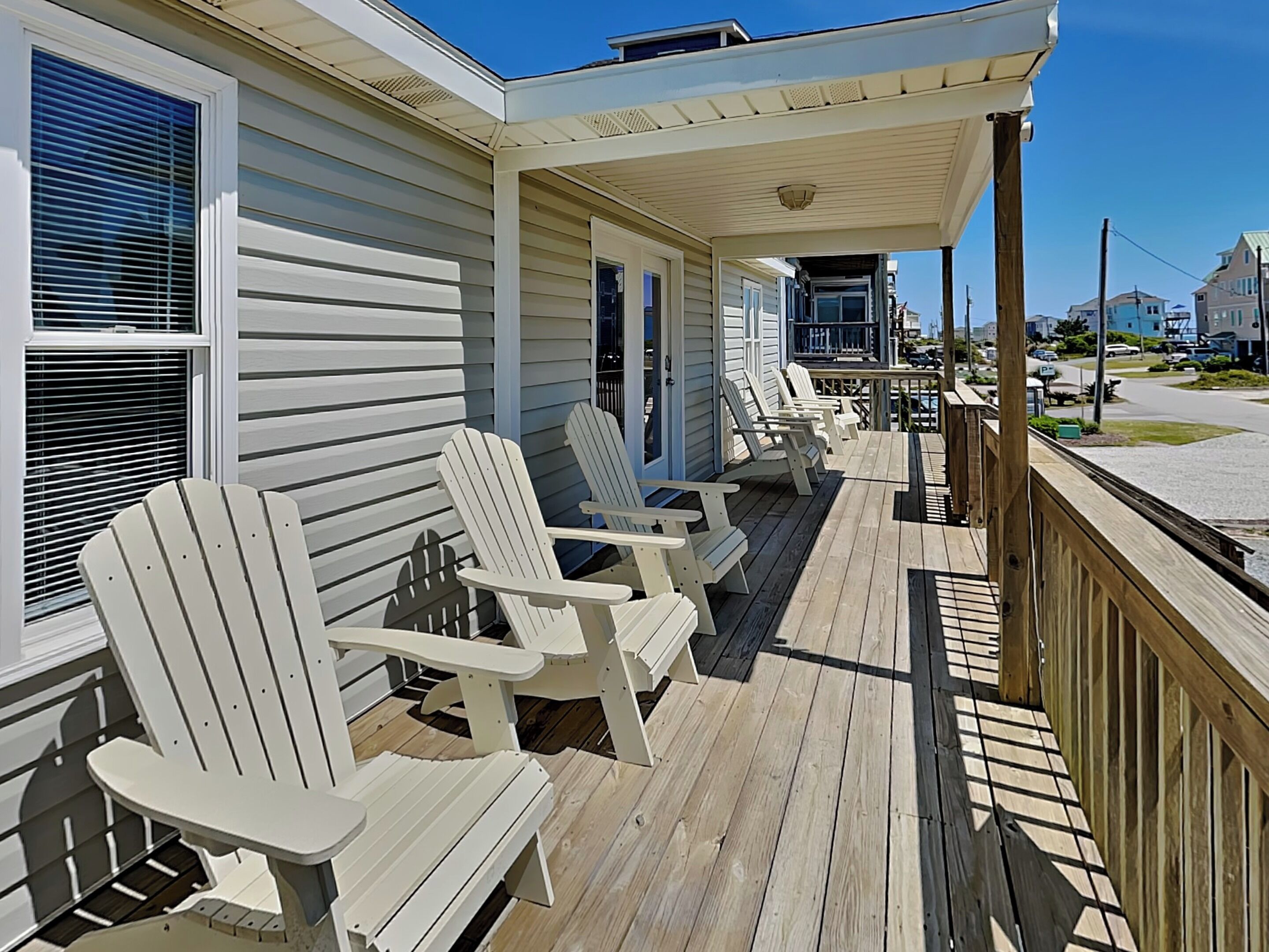 Een overdekte veranda met witte Adirondack-stoelen en een houten terras.
