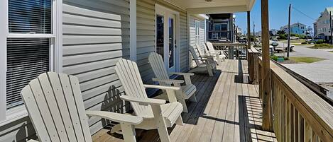 Een overdekte veranda met witte Adirondack-stoelen en een houten terras.