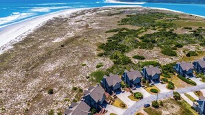 Vue aérienne d’une zone résidentielle côtière, avec des maisons, une plage et un ciel bleu dégagé.