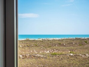 Strandudsigt med klart himmel og sandstrand med sparsom vegetation.