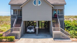 Une maison à deux étages avec un accès au garage, une voiture garée à l’intérieur et une vue sur la plage.