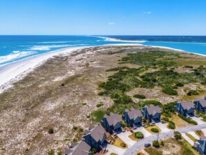 Vista aérea de una zona residencial costera con casas, una playa y un cielo azul despejado.