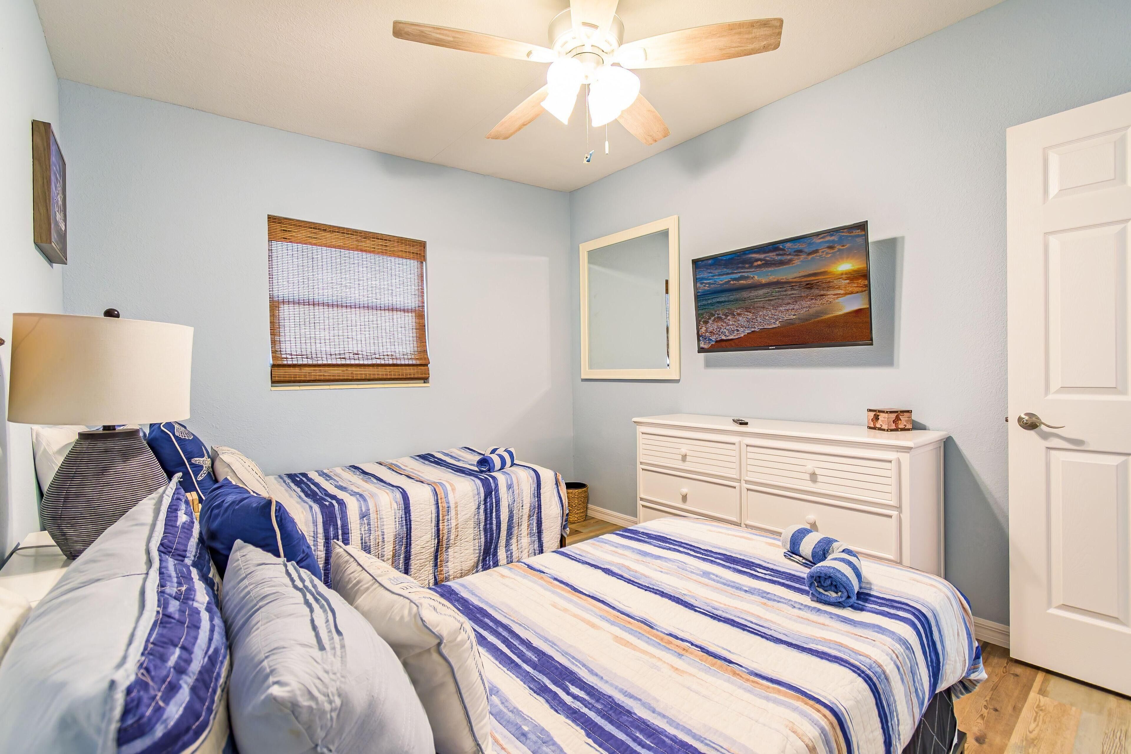 A bedroom with two beds, a ceiling fan, a dresser, a mirror, and a painting on the wall.