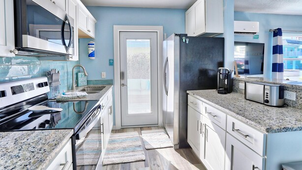 A modern kitchen with white cabinets, stainless steel appliances, and a granite countertop. - Shore La Vie (Treasure Island)