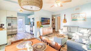 A spacious living room with a grey sofa, a wooden dining table with woven placemats, and a ceiling fan. - Shore La Vie (Treasure Island)