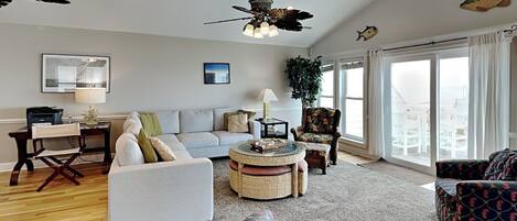 A spacious living room with a sofa, armchairs, a coffee table, and a ceiling fan.