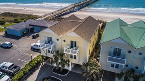A beachfront property with a pier extending into the ocean, featuring a parking area and multiple buildings with balconies. - Jolly Dave's by Topsail Realty (Holly Ridge)