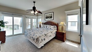 A bedroom with a large bed, a ceiling fan, a nightstand with a lamp, and a sliding glass door leading to a balcony. - Jolly Dave's by Topsail Realty (Holly Ridge)