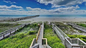 A beach with a wooden boardwalk leading to the water, surrounded by greenery. - Jolly Dave's by Topsail Realty (Holly Ridge)
