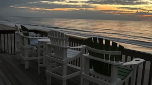 A wooden deck with white Adirondack chairs facing a beach at sunset. - Luna Escape by Topsail Realty (Holly Ridge)