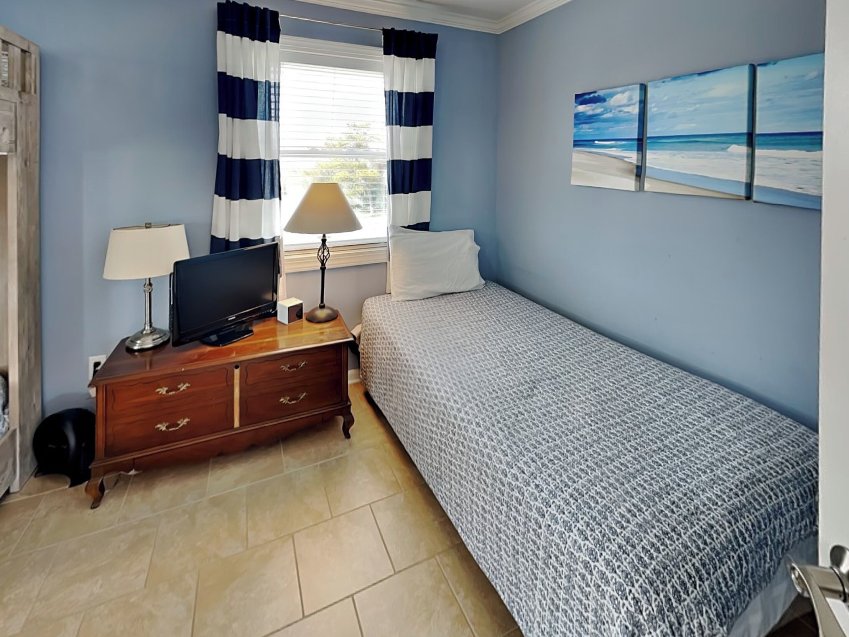 A room with a bed, a TV on a wooden dresser, a lamp, and a window with curtains.