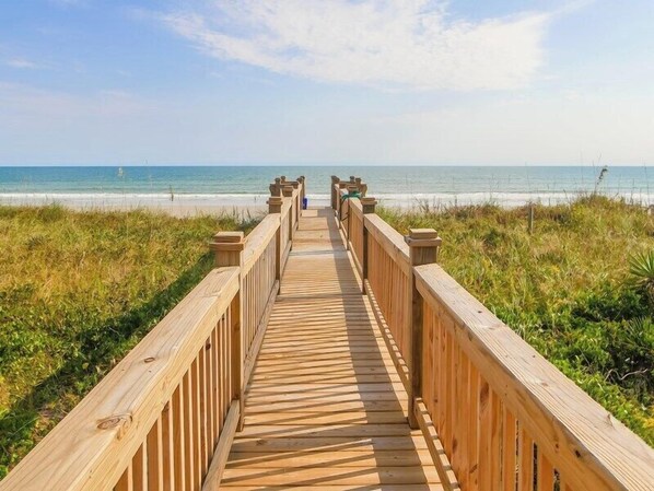 Walk along the boardwalk to the beach, flanked by lush grassy areas.