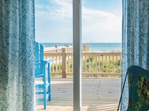 Enjoy a serene view of the beach from this room's spacious window, overlooking a deck with a chair and table.