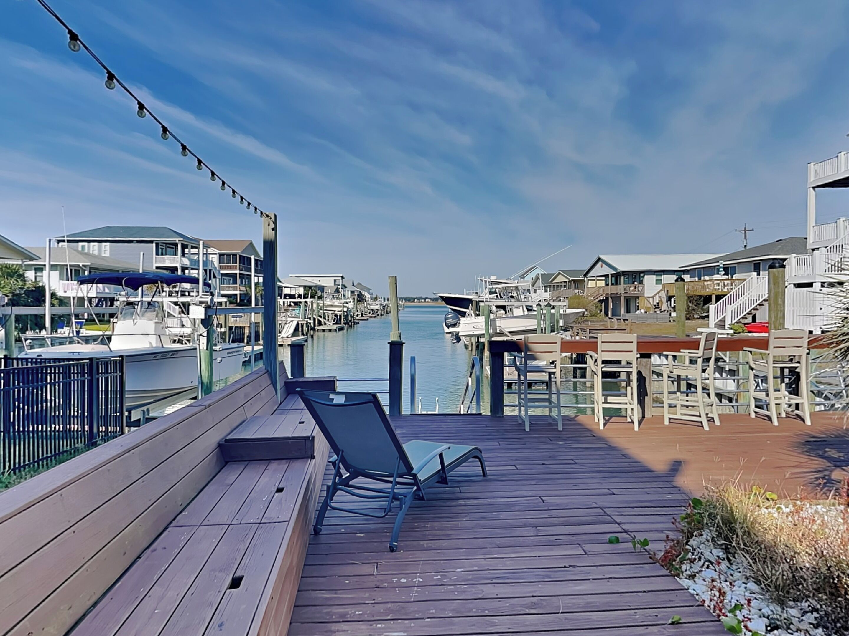 A wooden deck with a single lounge chair, overlooking a marina with boats and waterfront buildings.