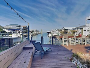 A wooden deck with a single lounge chair, overlooking a marina with boats and waterfront buildings.